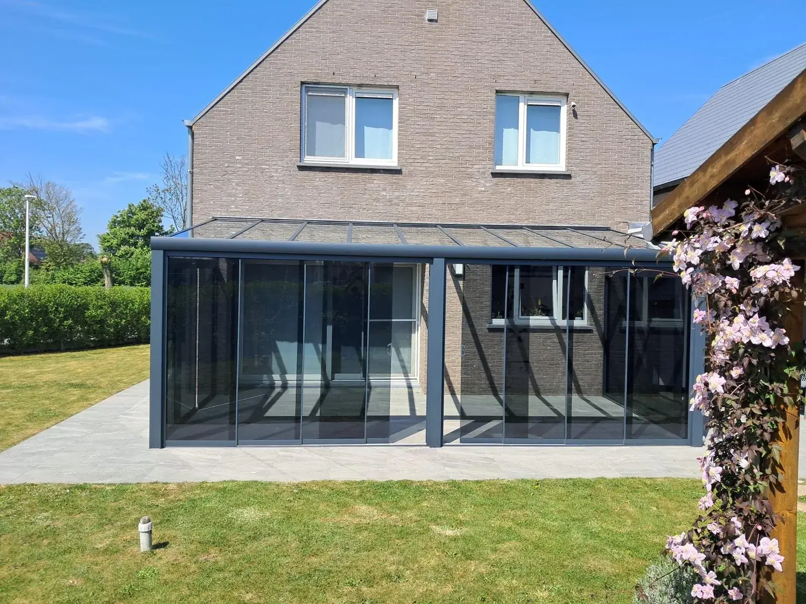 Anbau-Veranda mit getönter Verglasung und Glasdach an einem Backsteinhaus