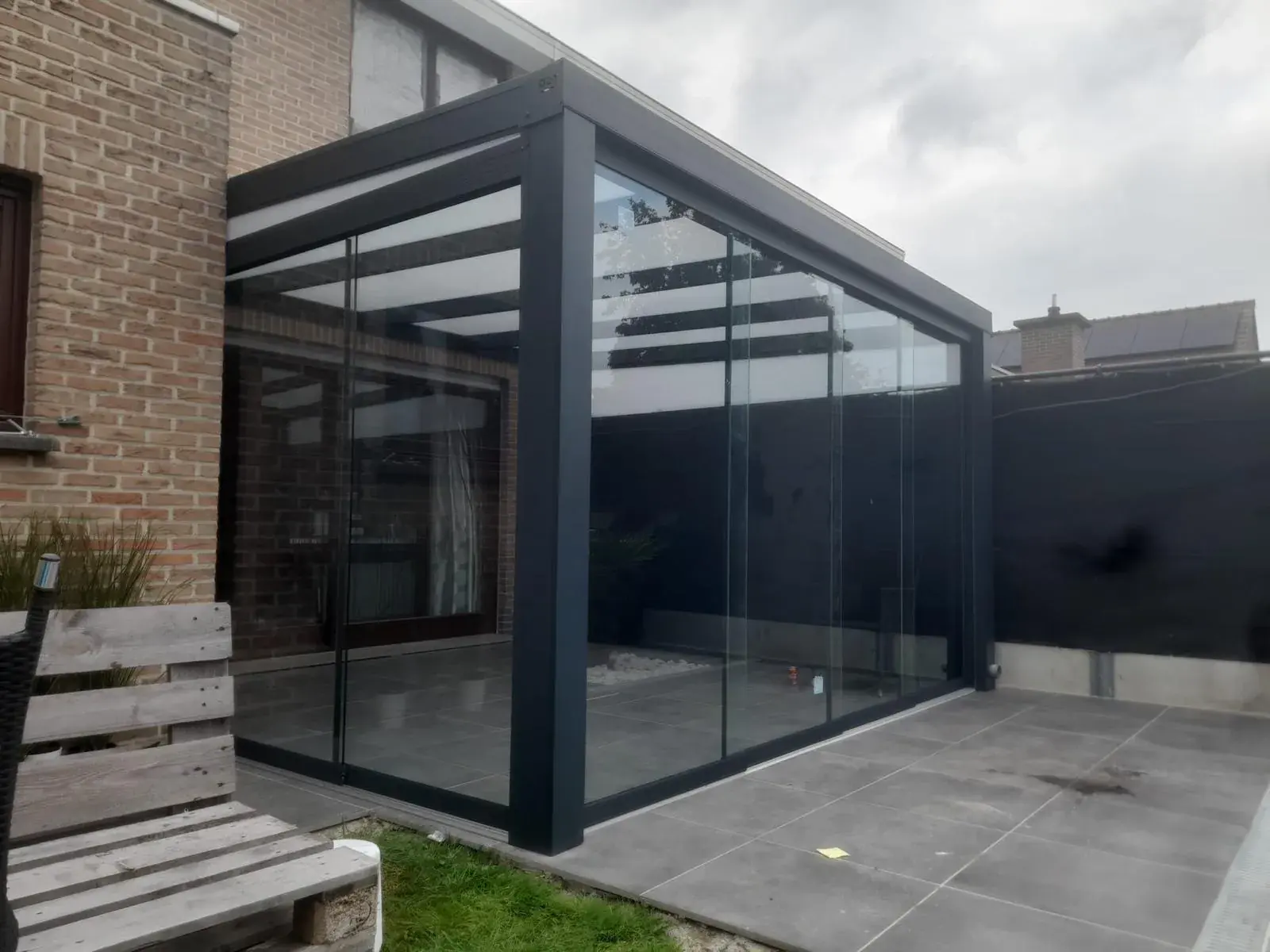 Anthrazitfarbene Veranda mit Glaswänden und lichtdurchlässigem Dach an einem Backsteinhaus
